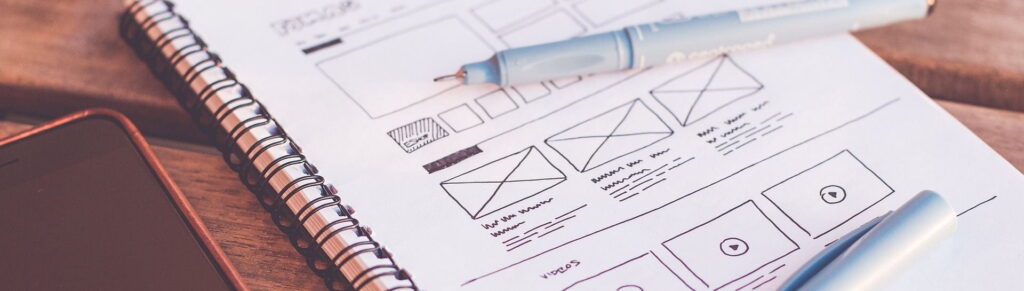 A pen and a notebook filled with wireframe sketches of web page designs.
