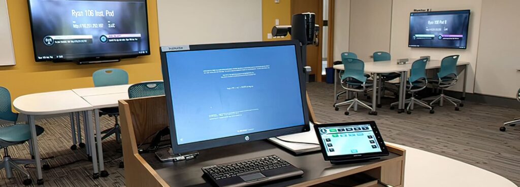 A classroom showing several computer monitors, a large LED display and a smaller room controller